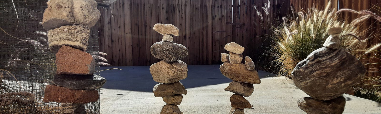Some vertical stacks of rocks at the edge of a paved area. The stacks look like they might tip over.