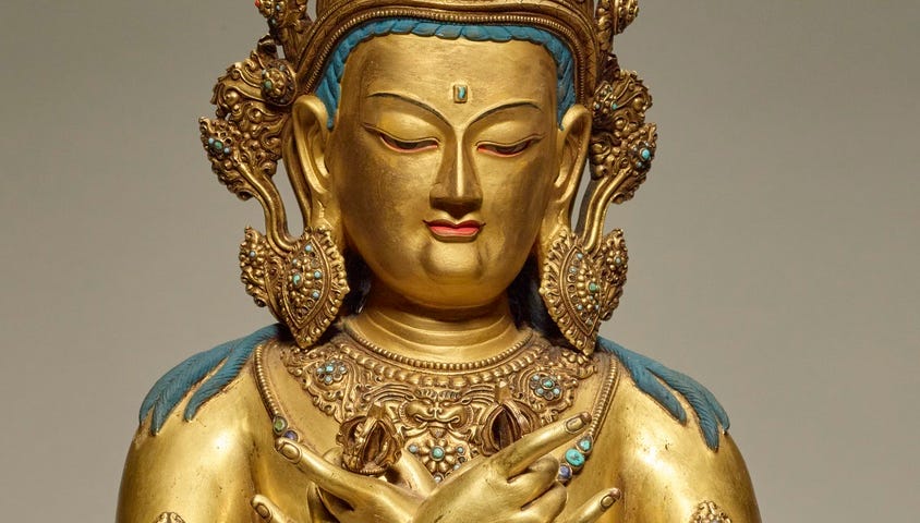 A golden figure of a Buddha, with a large golden crown, hands crossed on its chest.