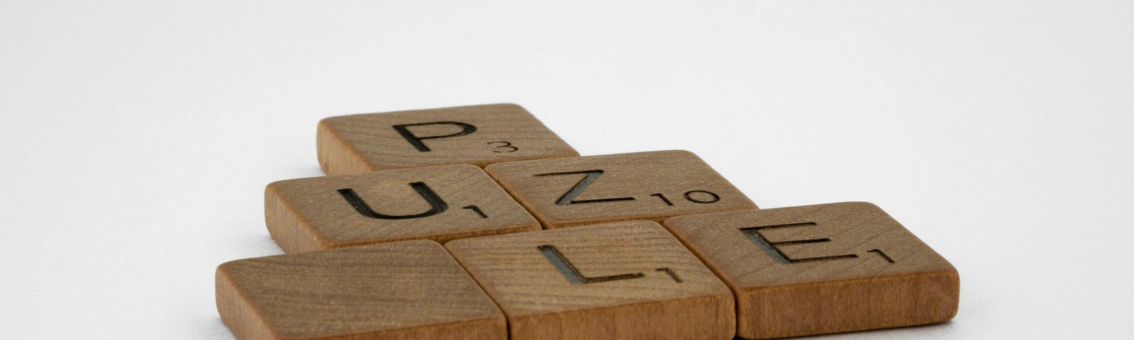 Scrabble tiles are arranged into a flat pyramid, spelling “puzzle” without the second “z.”