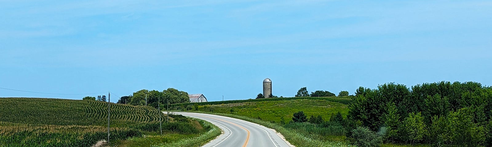 This shows a road with a curve with open fields on both sides.