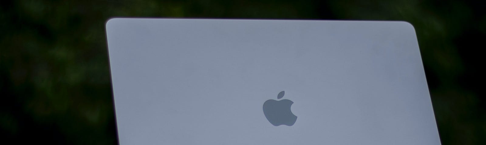 An M1 MacBook Pro 13" sitting backward atop its box which is resting on a red velvet sheet contrasted with a dark background.