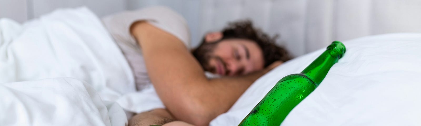 Man asleep with beer bottle on a pillow and phone in hand