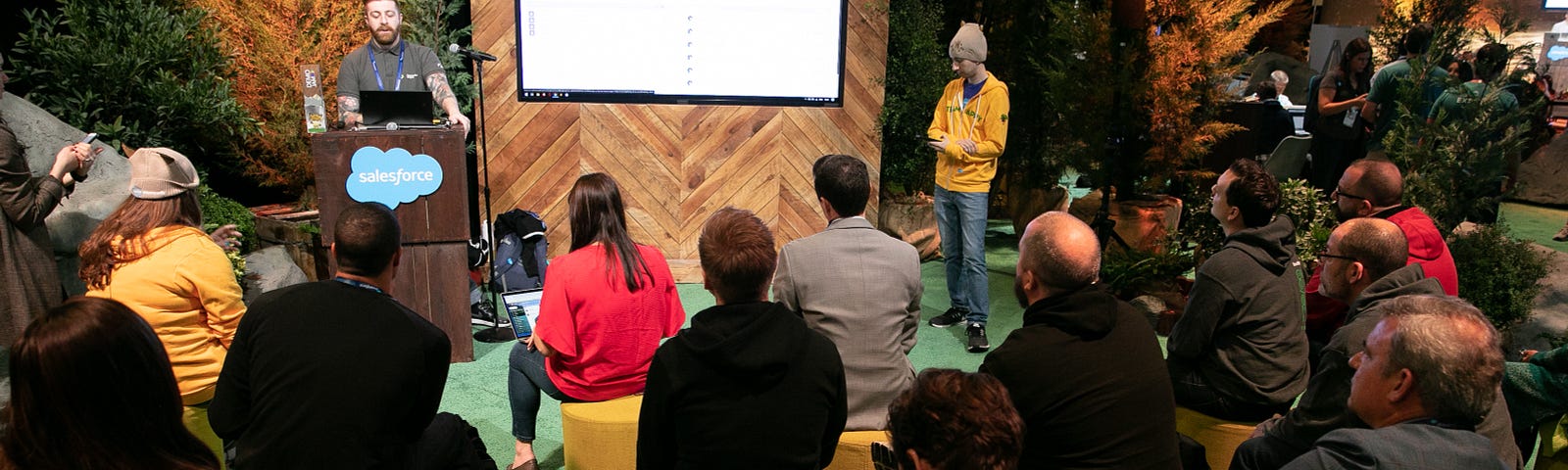 Several people sitting on yellow ottomans and listening to a Salesforce partner speak about AppExchange.