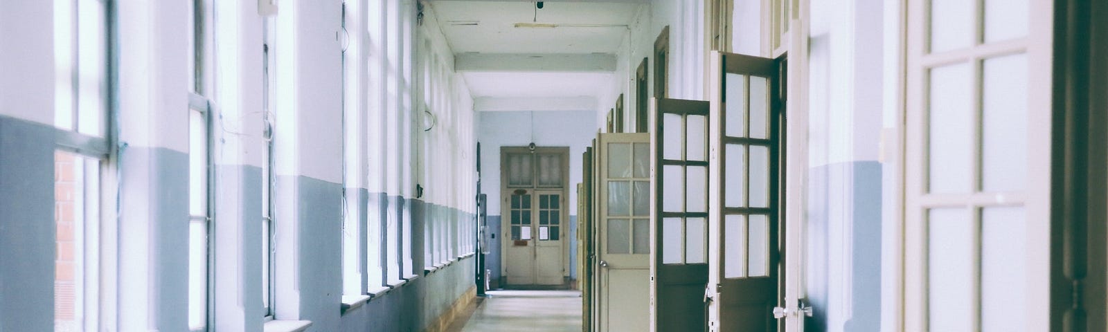 A hallway with slightly open doors of different muted colors where the paint is chipping on the walls.