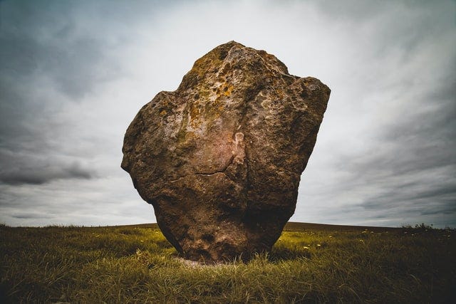 A rock with cloudy sky and grassy field