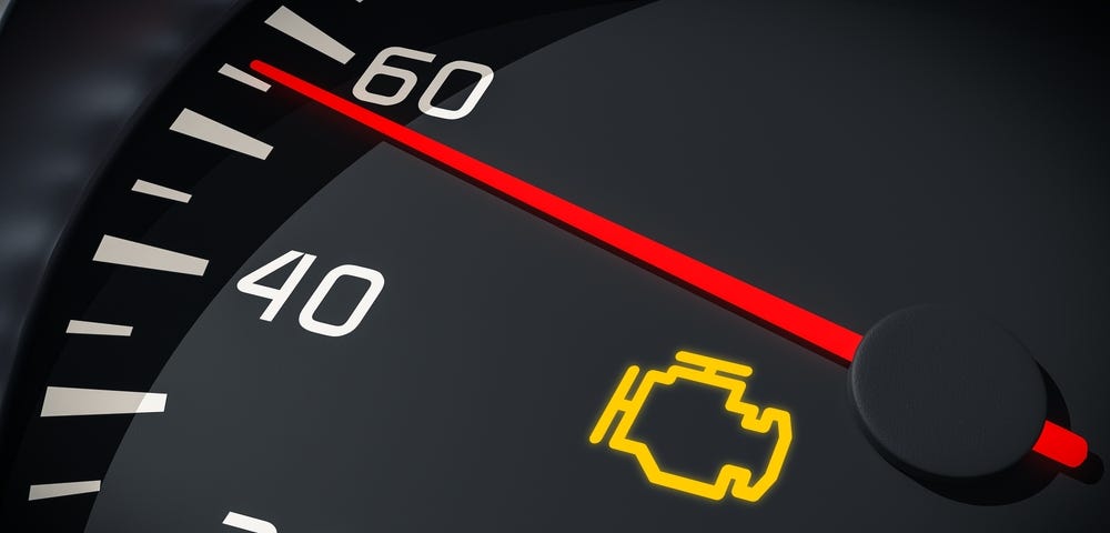 A car dashboard speedometer showing the check engine warning light