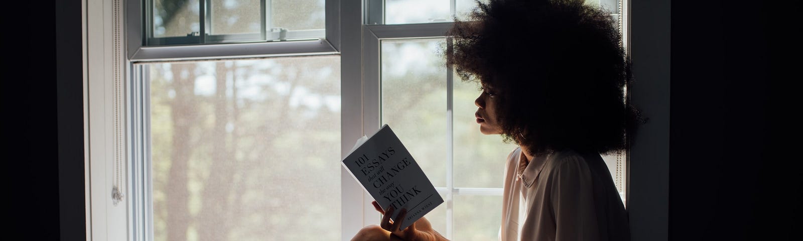 A girl reading a book by the window.