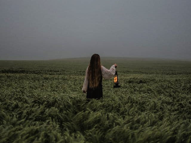 A woman holding a lantern standing in a field on a dark day.