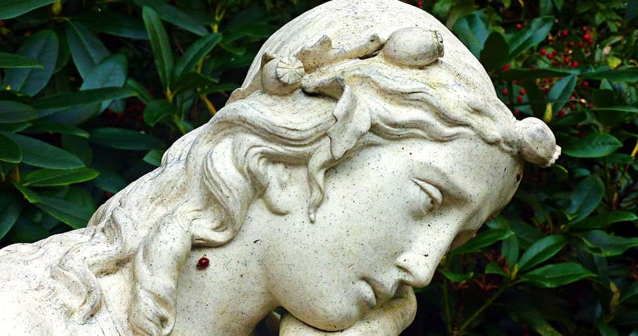 A statue of an angel looking exhausted, with her head in her hand.