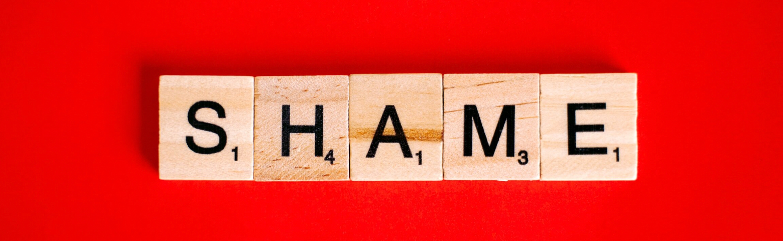 Scrabble tiles spell out the word “Shame” on a red background.