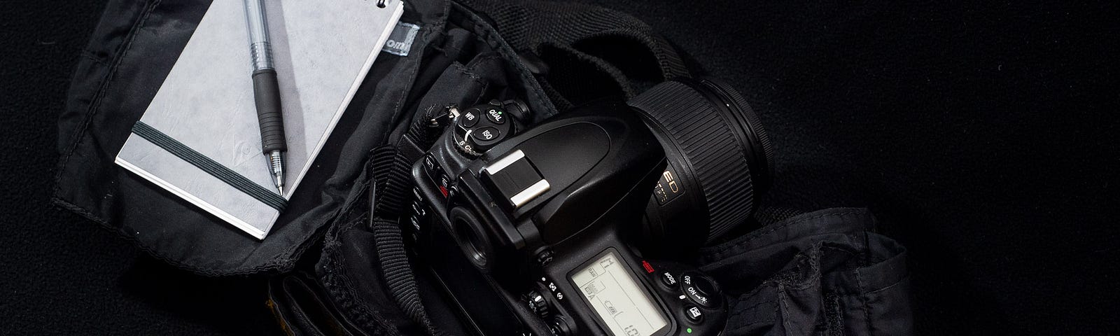 A display of a DSLR camera and a paper notebook sitting on a camera bag.