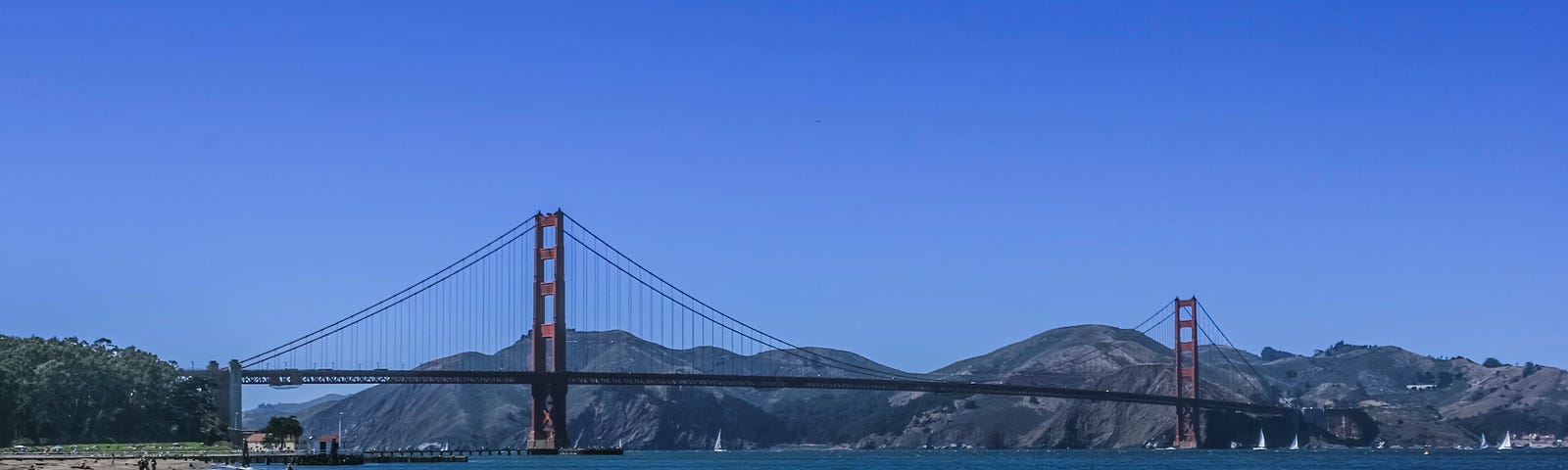 The Golden Gate Bridge in San Francisco Bay. A rocky beach is in the foreground and the Marin hills are behind the bridge.