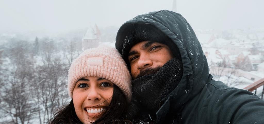 Gabrielle e João, fortemente agasalhados, posam abraçados sob a neve na Old Town, em Tallinn.