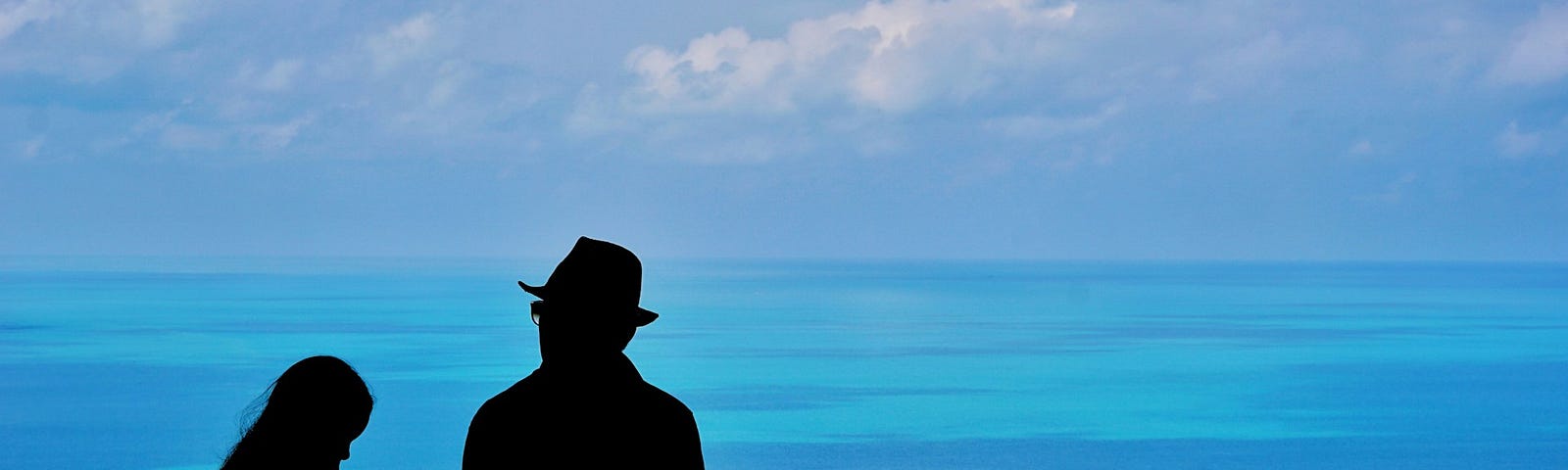silhouette of a man and girl against a blue sky and seascape