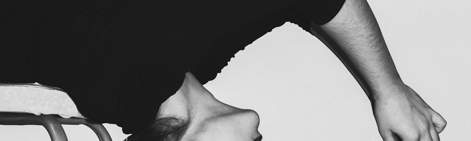 Woman leans backwards on a chair and looks at a paper flower in her hand. Black and white.