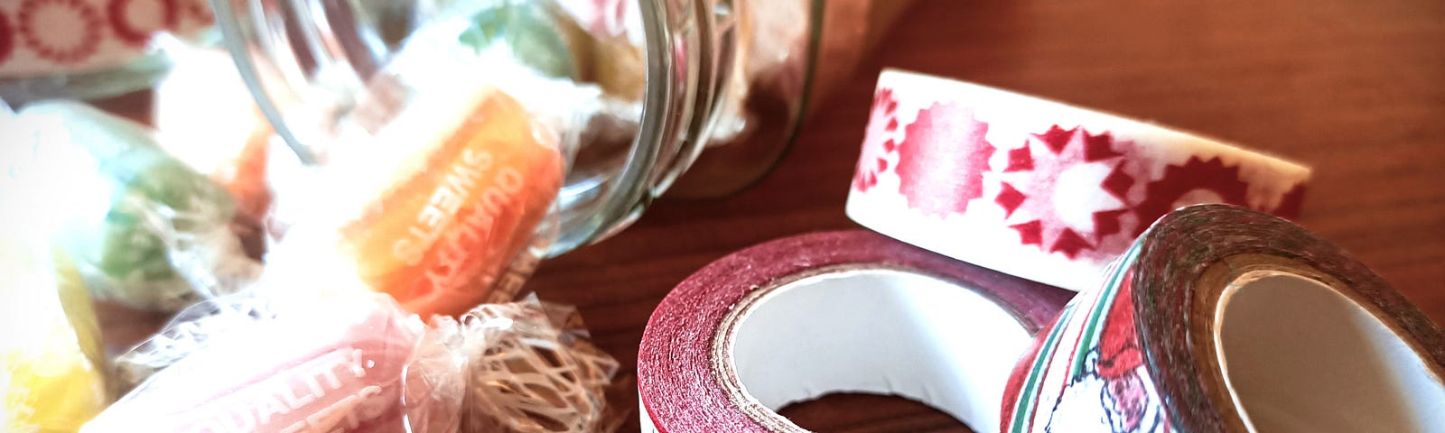 A jar with coloured sweets tumbling out is next to three rows of Christmas sticky tape.