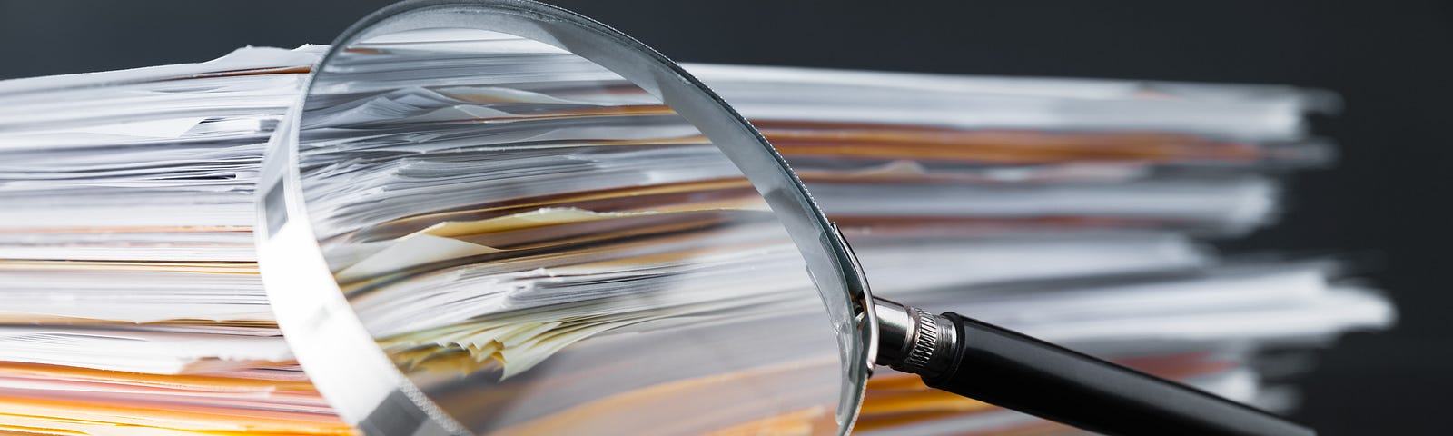 A magnifying glass leaning against a stack of reports. Photo by Sezeryadigar/Getty Images