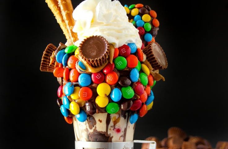 A colourful milkshake full of M&Ms and chocolates along with whipped cream and thick chocolate ice cream.