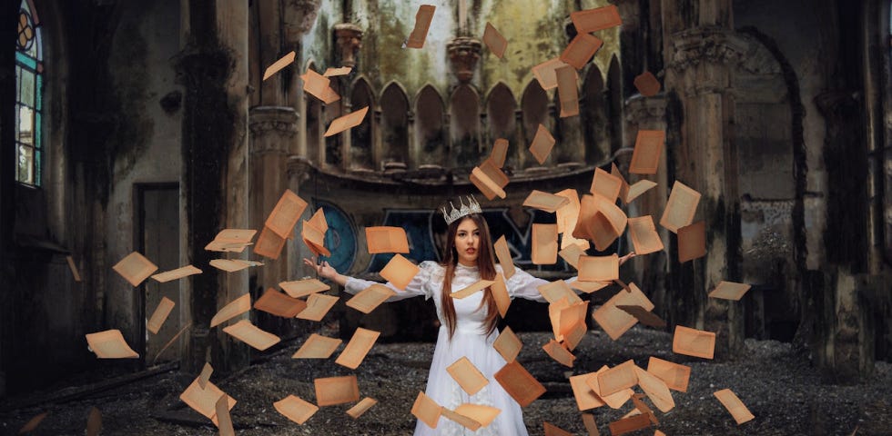 A woman wearing a lopsided crown and a white satin dress with pages from a book swirling around her.