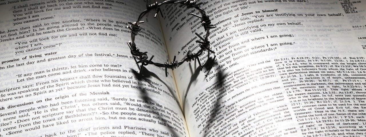 An open book and resting on the open pages is a ring of thorns, which casts a shadow of a heart on the pages.