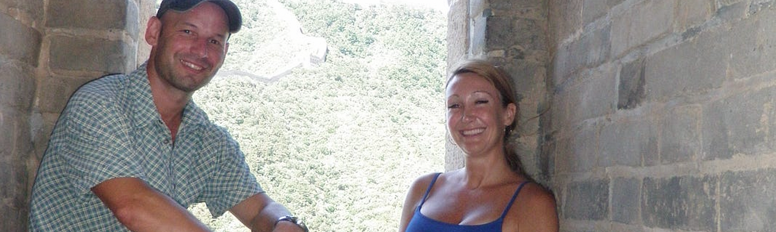 A man and a women sitting in front of a large open window. The great wall is visible in the background snaking off into the distance