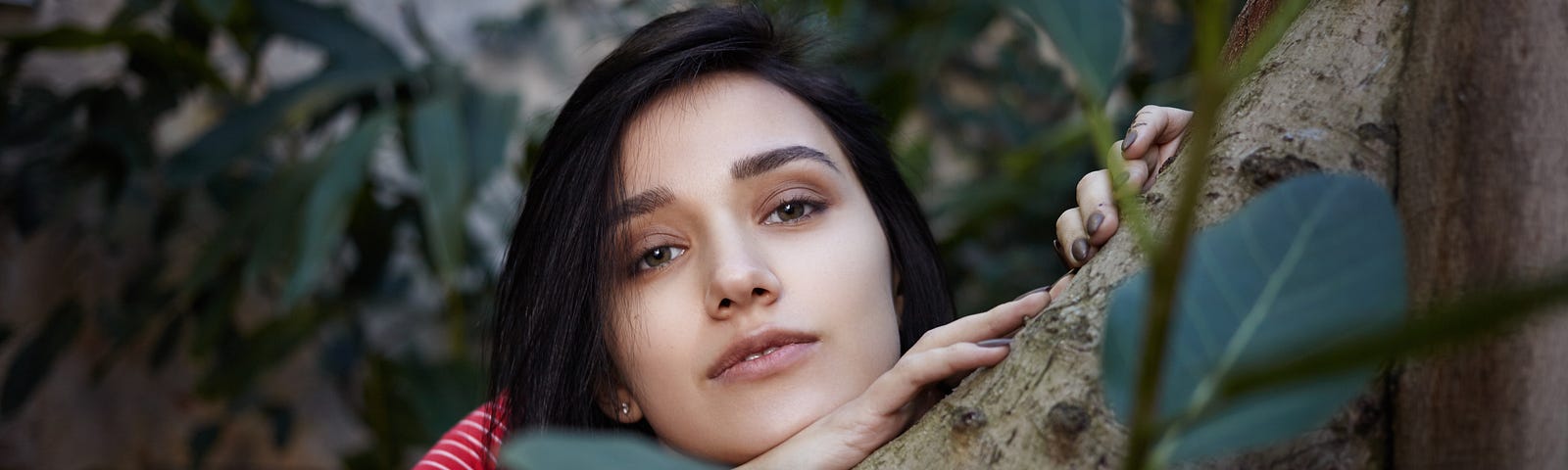 Woman leaning on thick trunk of tree