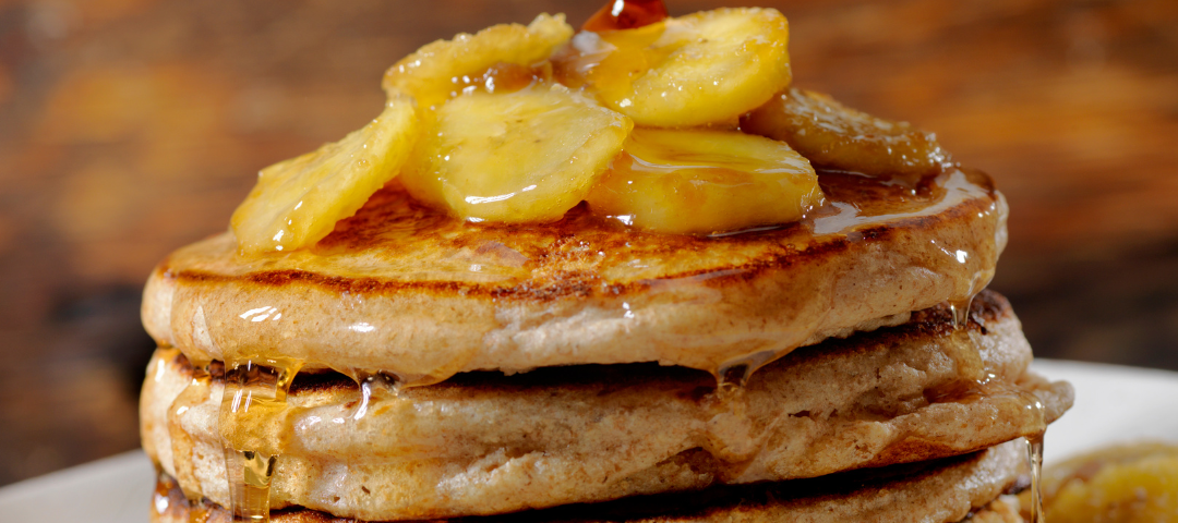 A stack of pancakes with carmelized bananas and maple syrup