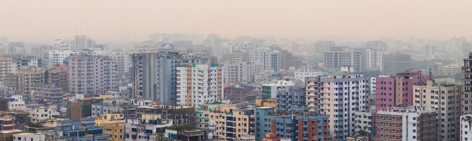 Landscape image of the city of Dhaka, Bangladesh, featuring high rise buildings and a hazy sky.
