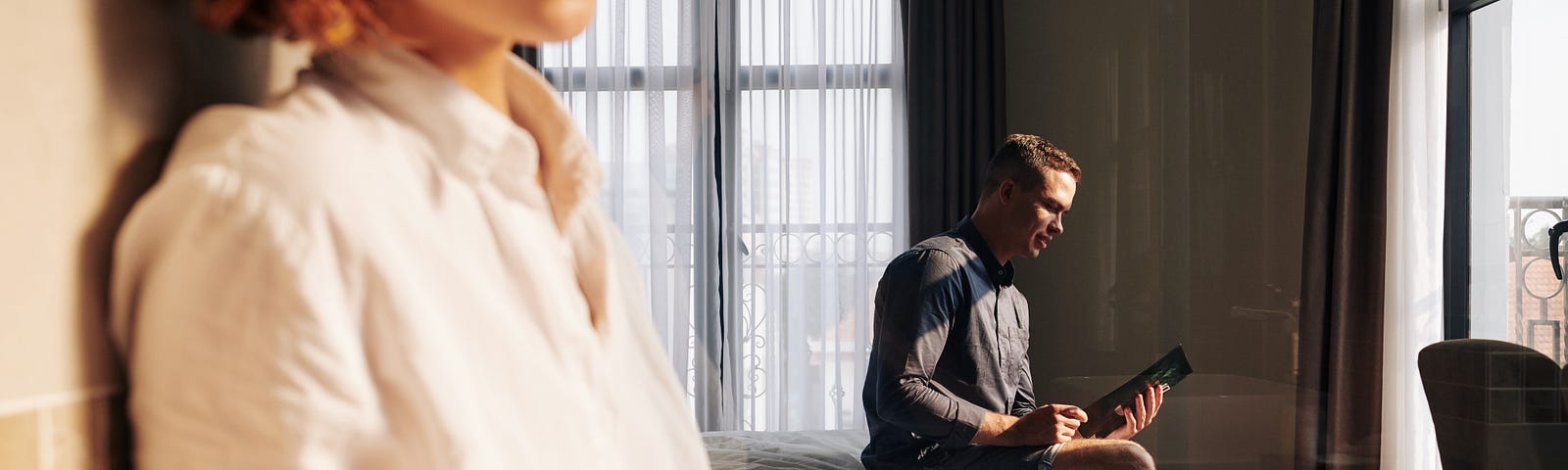 A lonely woman sits separate from her partner who stares into his phone on the other side of the room.