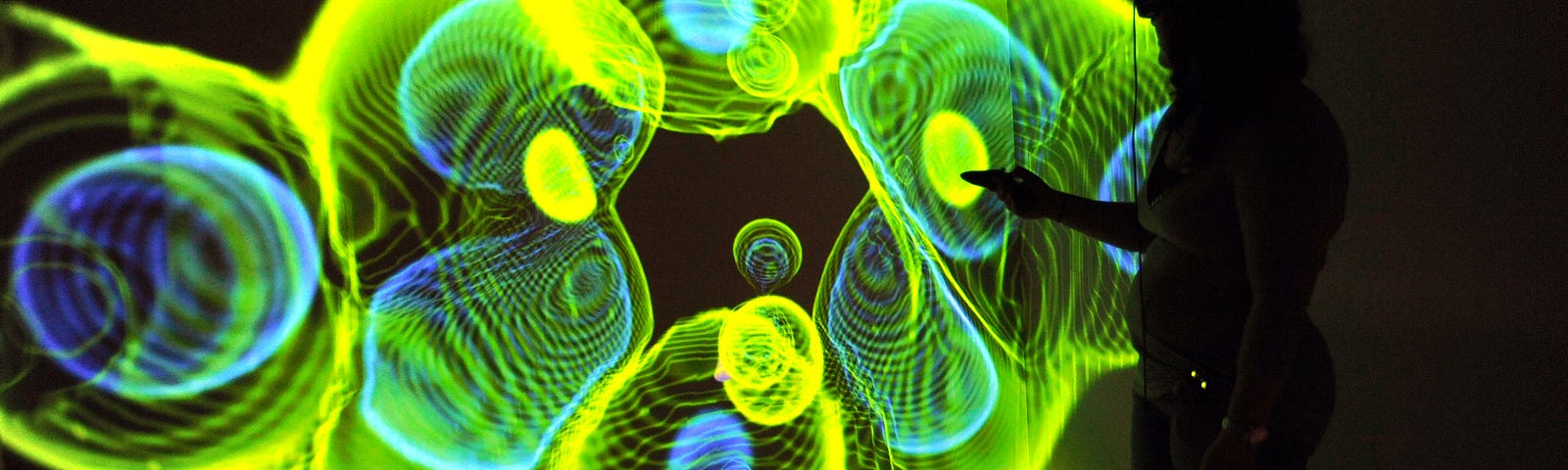 The image shows the silhouette of a person in front of a yellow, green and blue “jellyfish” representation of data.