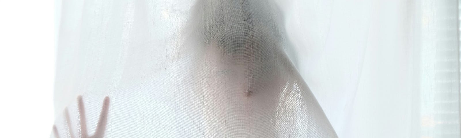 Woman behind a white gauze curtain.