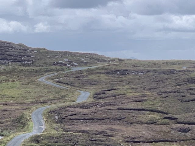 a long, winding single track road over deserted heath with the sea in the distance