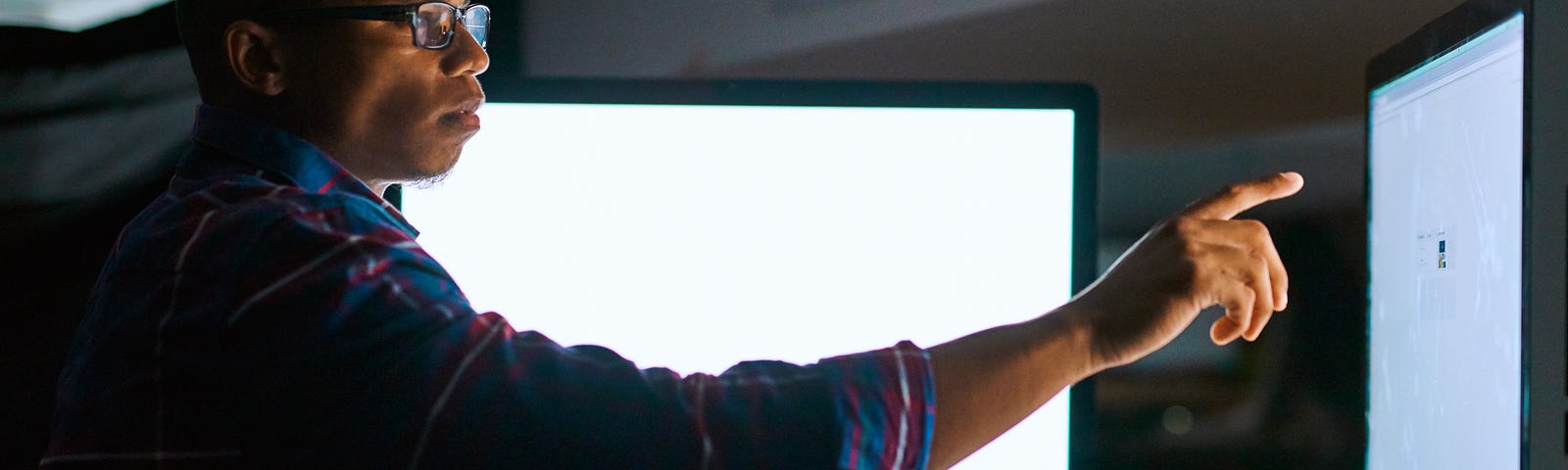 Man pointing at a computer screen in a darkened room. Photo by PeopleImages/Getty Images