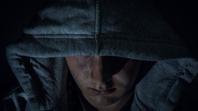 Threatening, male with a hoodie pulled low to partially obscure his face - dark, menacing, sombre