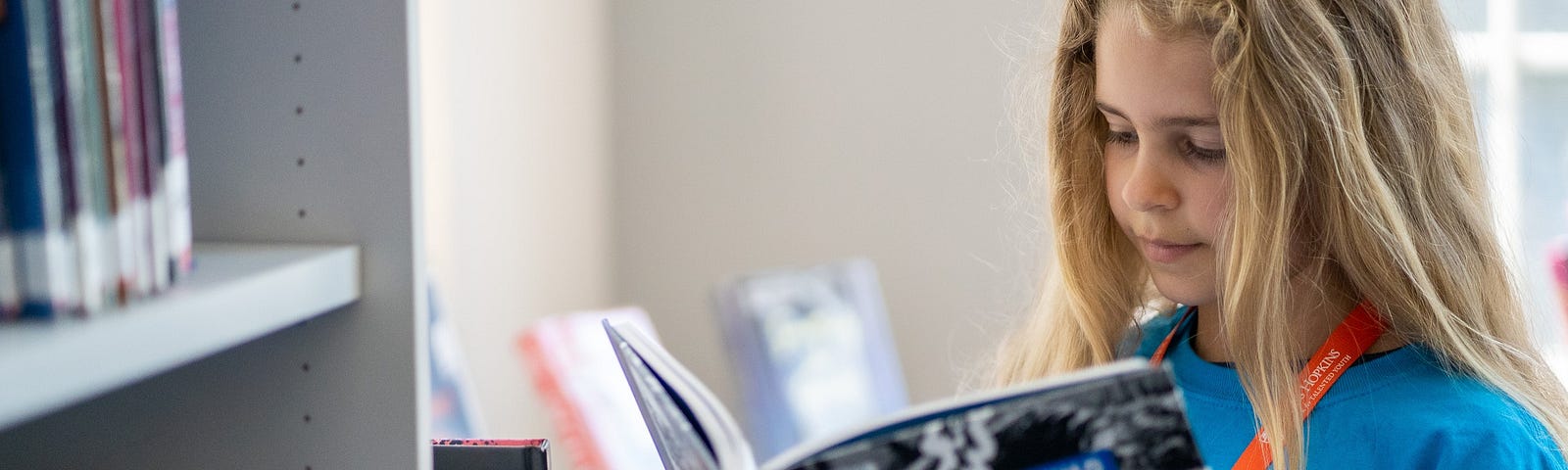 An image of a CTY student reading a book in front of a bookshelf.