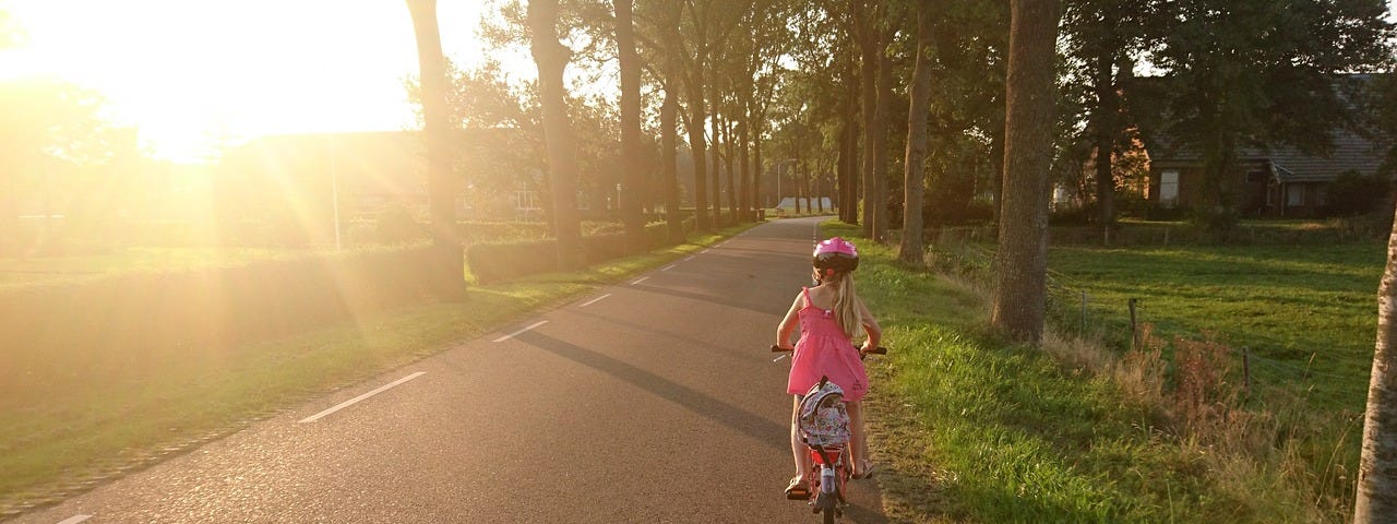 A young girl riding her bike along the side of the road.