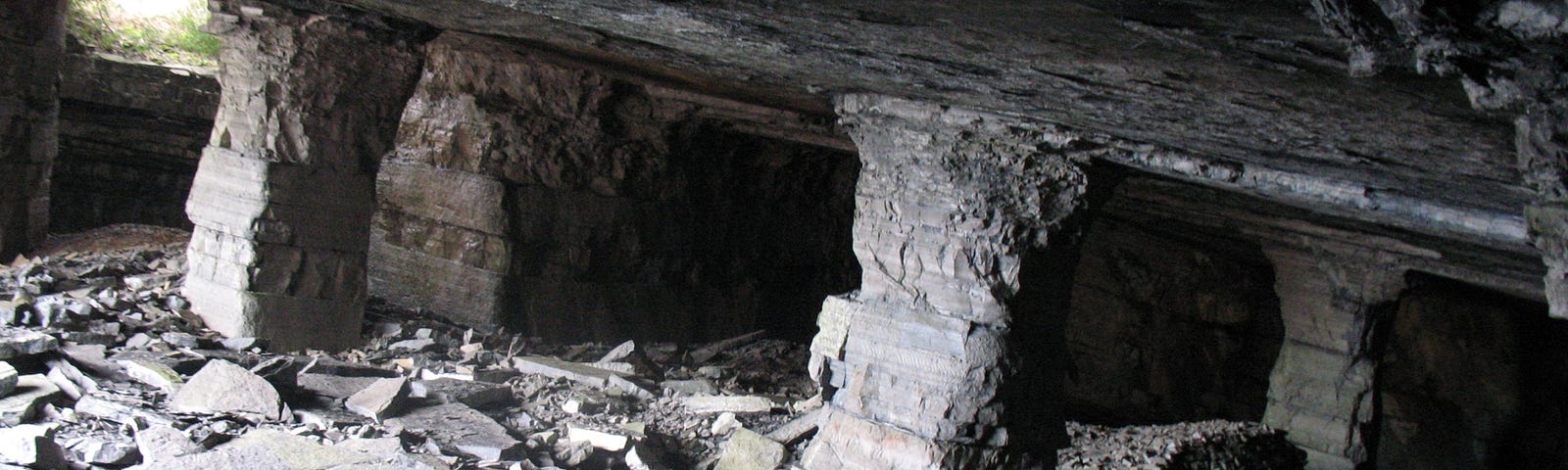 Underground passage with small window of light, four eroded columns and fallen tile mixed with rubble