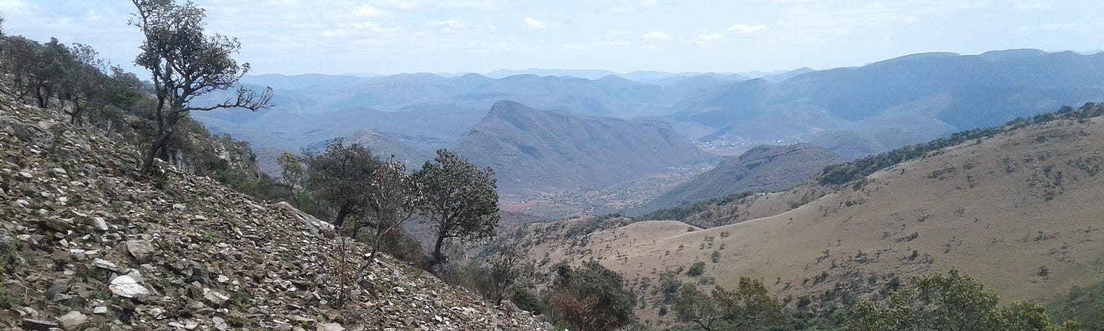 A rocky hill on the left and a grassy plain on the right, with mountains in the background