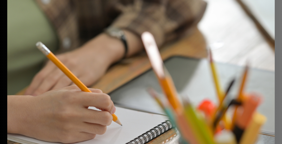 Hands on the desk, one writing with a pencil