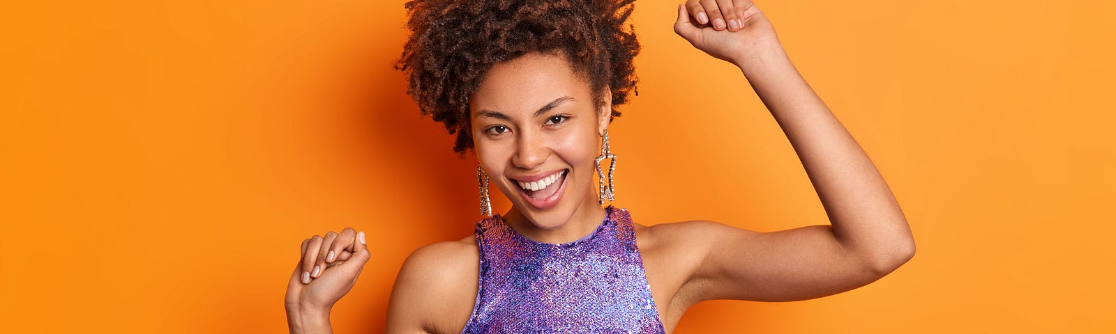 Woman in shiny top dancing and having fun against orange backdrop