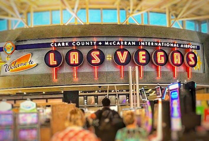 A photo in Las Vegas McCarran airport with its bright, neon Welcome to Las Vegas sign, slot machines and people walking