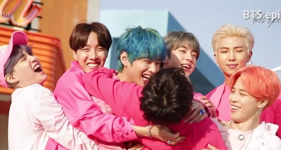 BTS members embrace each other with large smiles on their faces.