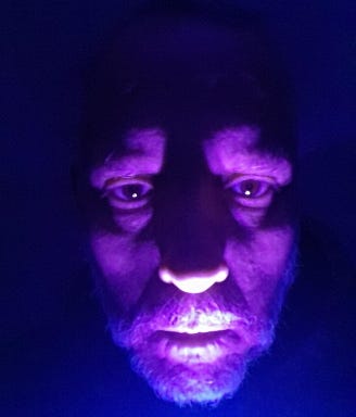 Author’s face, lighted from beneath by UV light, at night.