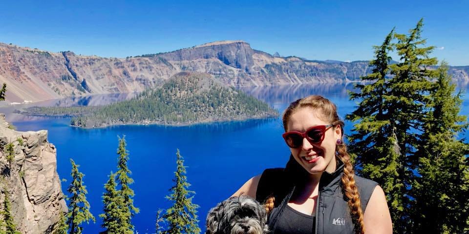 Deanna with her dog on a cliff overlooking a lake and mountains.