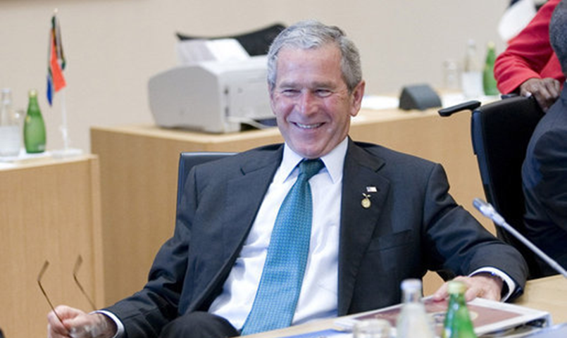 Former President George W. Bush sitting at a table smiling.