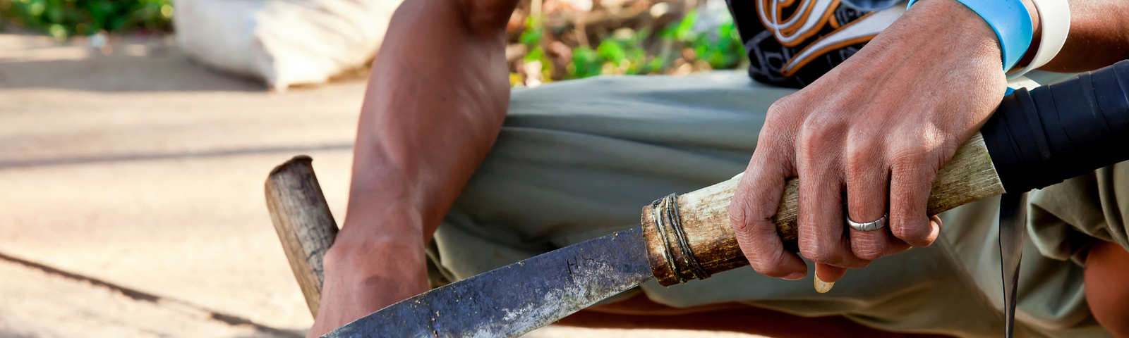 man crouching, holding machete and wood