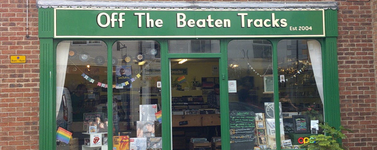 Image of the shop frontage of a music shop in Louth, Lincolnshire called ‘Off The Beaten Tracks’ with windows decorated with merchandise and potted plants situated outside on the pavement.