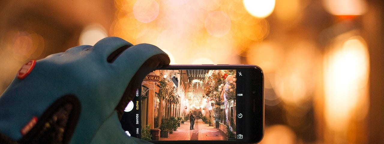 A person is holding an iPhone showing a Christmas decorated street.