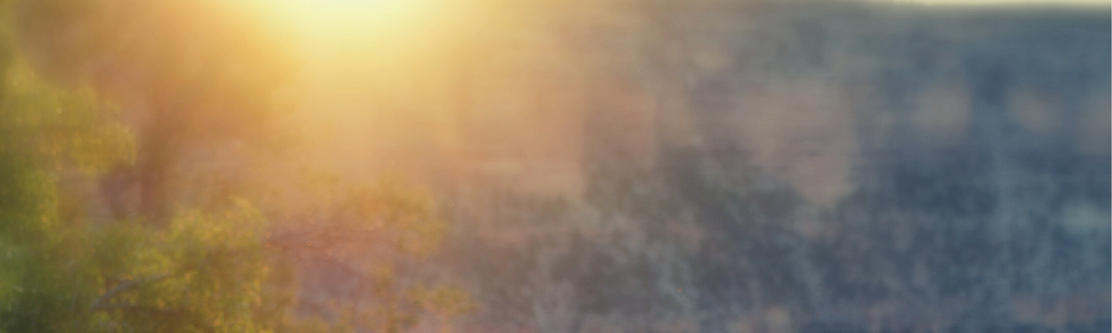 A dreamy, bright setting sun disappearing beneath a canyon’s rim.