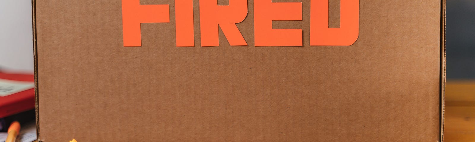 Photo of the side of a cardboard box with the word FIRED cut out from orange construction paper. In front of the box are wadded up stickies.